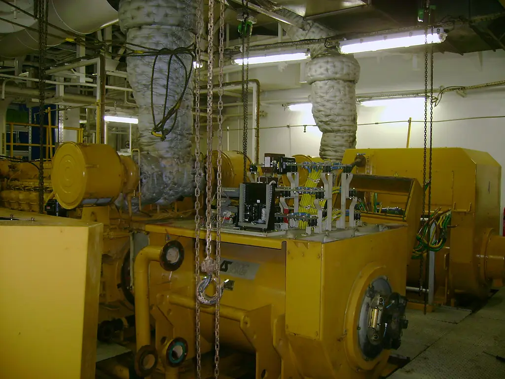 Yellow generator set in an engine room, the alternator in the foreground